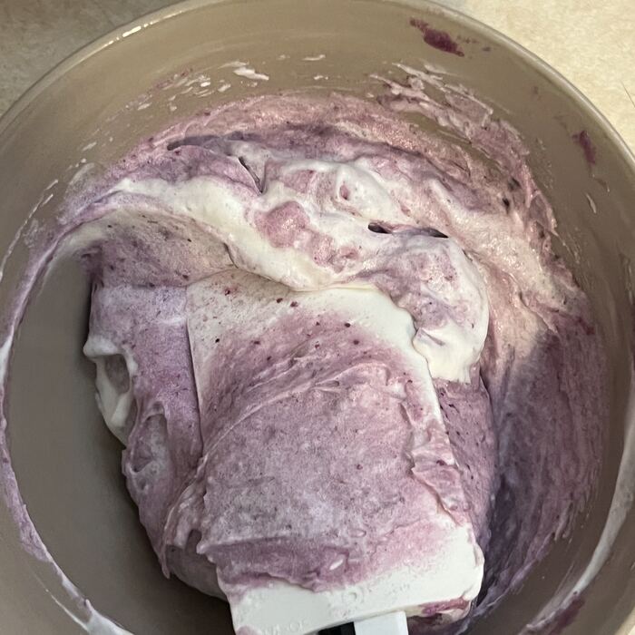Ube halaya being folded with a spatula in a steel pot