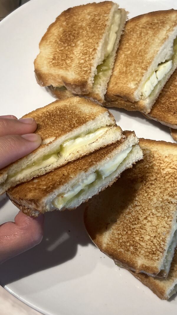 A hand lifting a piece of kaya toast above a plate
